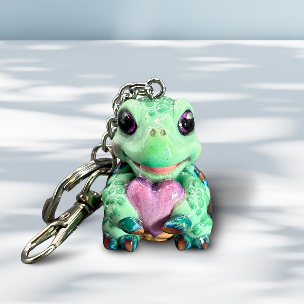 Cute baby sea turtle holding a purple heart keychain.