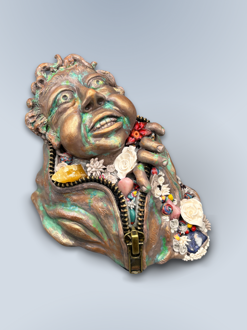 Hand made sculpture using Polymer clay, depicting a happy face exiting from a giant suit. This sculpture is painted to look like patinaed bronze and is decorated with natural stone, gems and sculpted flowers.