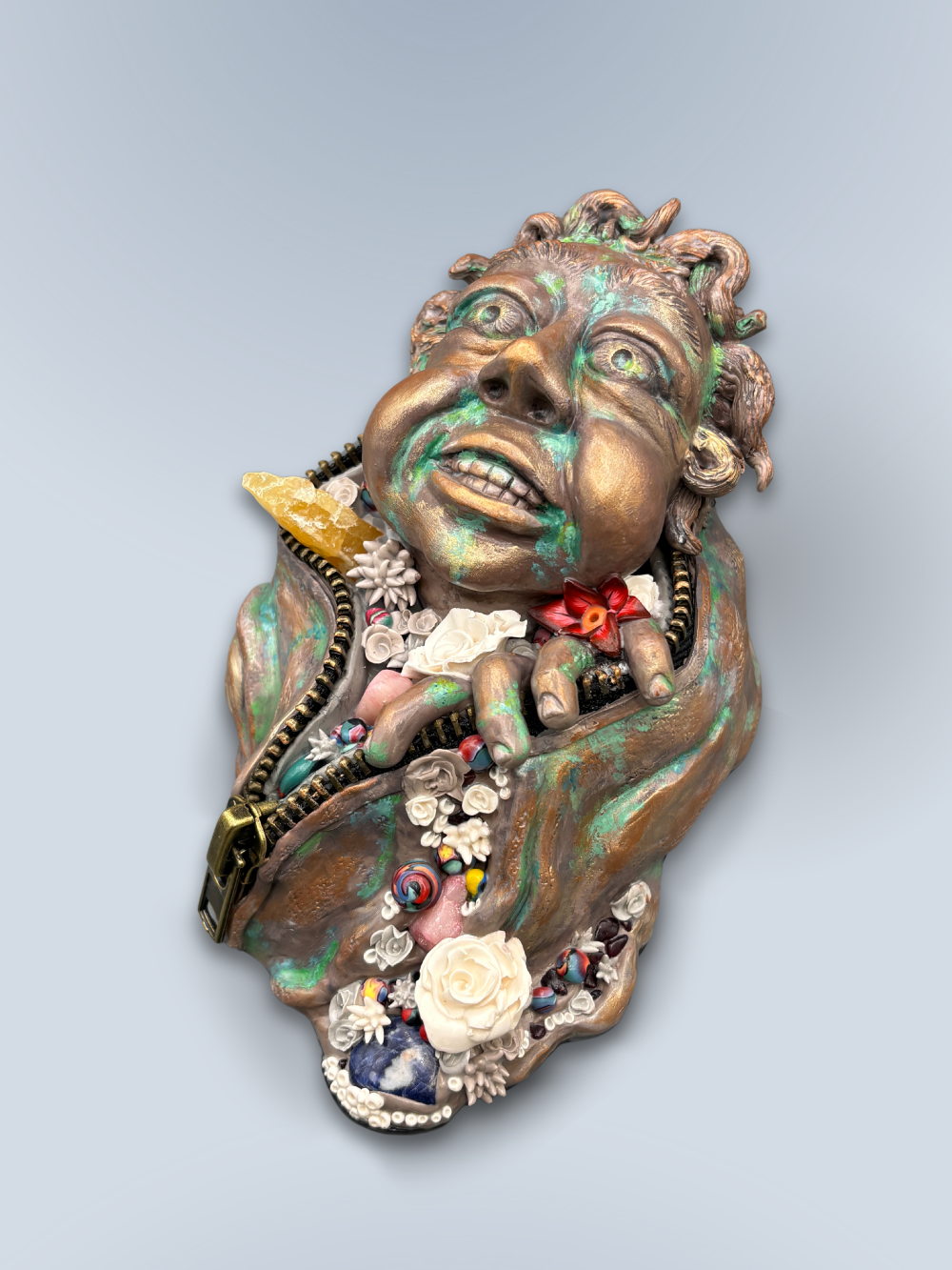 Hand made sculpture using Polymer clay, depicting a happy face exiting from a giant suit. This sculpture is painted to look like patinaed bronze and is decorated with natural stone, gems and sculpted flowers.