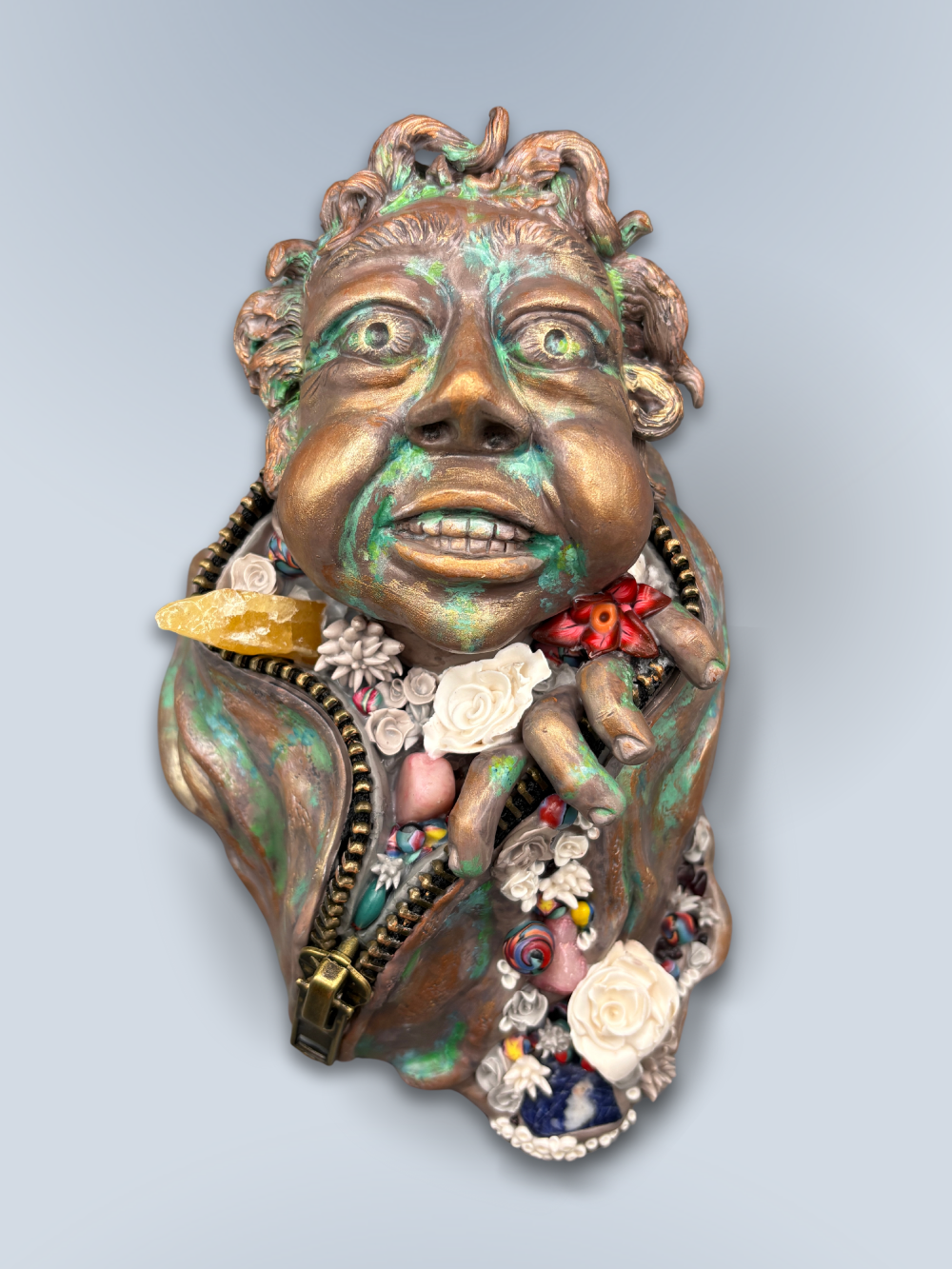 Hand made sculpture using Polymer clay, depicting a happy face exiting from a giant suit. This sculpture is painted to look like patinaed bronze and is decorated with natural stone, gems and sculpted flowers.