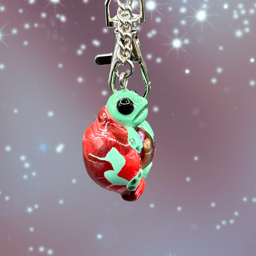 Green and red turtle keychain with a blue marble in its belly