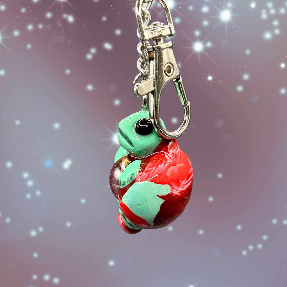 Green and red turtle keychain with a blue marble in its belly
