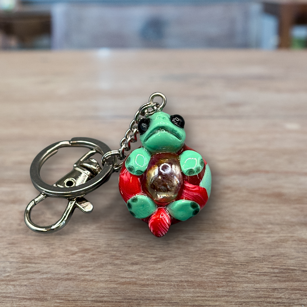 Green and red turtle keychain with a blue marble in its belly
