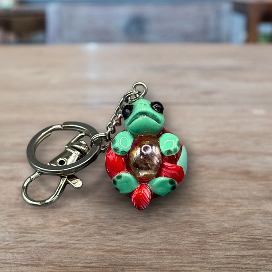 Green and red turtle keychain with a blue marble in its belly