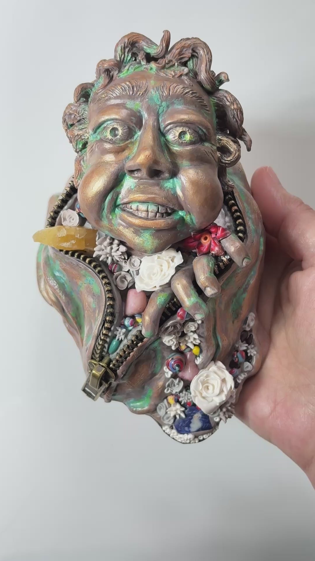 Hand made sculpture using Polymer clay, depicting a happy face exiting from a giant suit. This sculpture is painted to look like patinaed bronze and is decorated with natural stone, gems and sculpted flowers. 